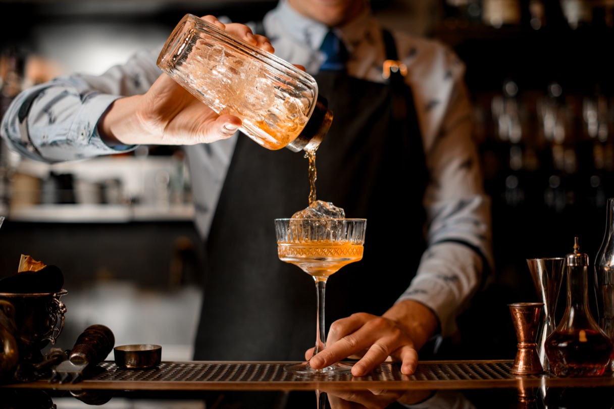 A bartender pouring a cocktail at a bar.