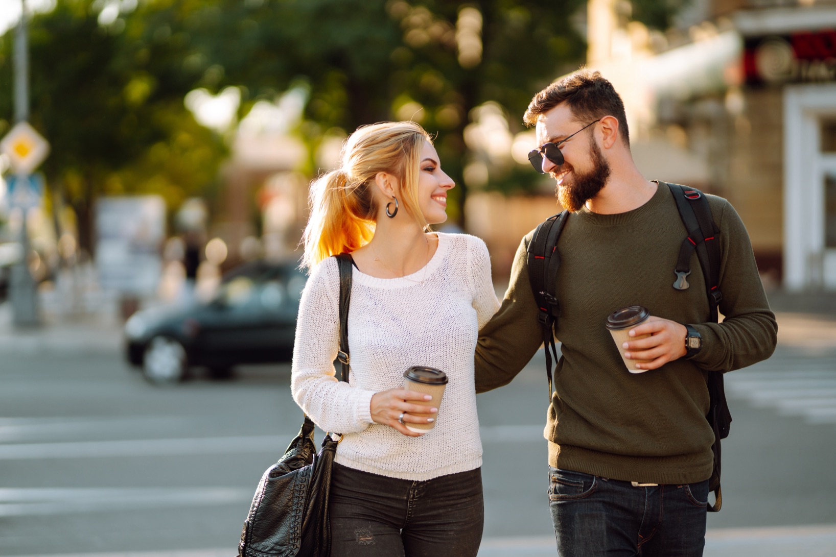 Two people walking with takeaway coffees along a suburban shopping street.